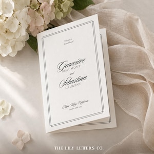 May include: A white folded wedding programme card featuring a black double-line border and elegant black typography. The text reads: Welcome to the wedding of Geneviève Beaumont and Sebastian Laurent, Napa Valley, California, October 18th, 2017.