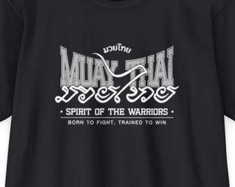 May include: Black t-shirt with a white graphic design. The design includes the words "Muay Thai" in a stylized font, along with text in a foreign language and the phrases "Spirit of the Warriors" and "Born to Fight, Trained to Win."