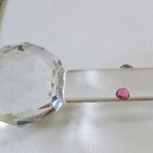 May include: A clear glass rod with a crystal end and a metal end with a decorative design. The rod is decorated with pink dots.