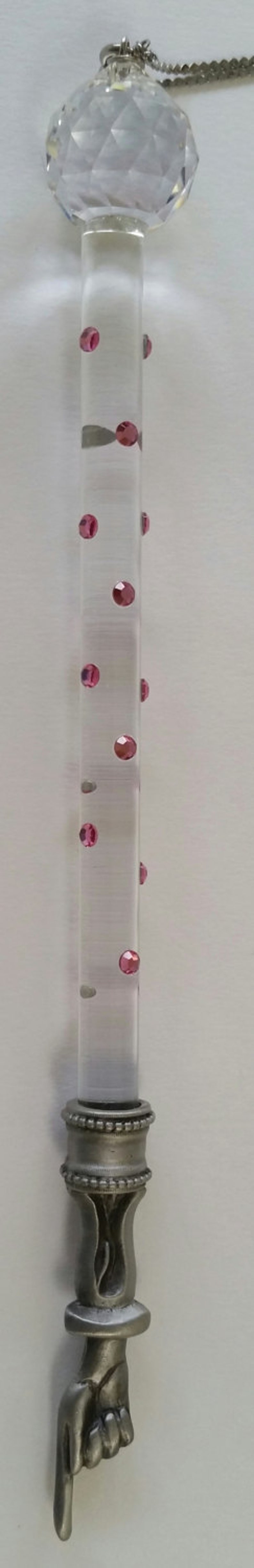 May include: A clear glass crystal ball with a silver chain attached to a silver base with a hand-shaped design. The glass tube contains pink glitter.