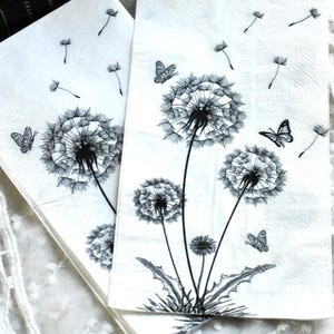May include: White paper napkins with a black and white dandelion design. The napkins feature detailed illustrations of dandelions, butterflies, and floating seeds, creating a nature-inspired theme.