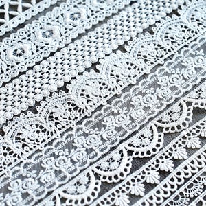 May include: Close-up of several white lace trims with various floral and geometric patterns. The trims are arranged diagonally, showcasing different designs, including floral, scalloped edges, and openwork details. Ideal for sewing and craft projects.