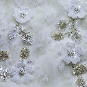 May include: White lace fabric with delicate floral appliques and silver beading.