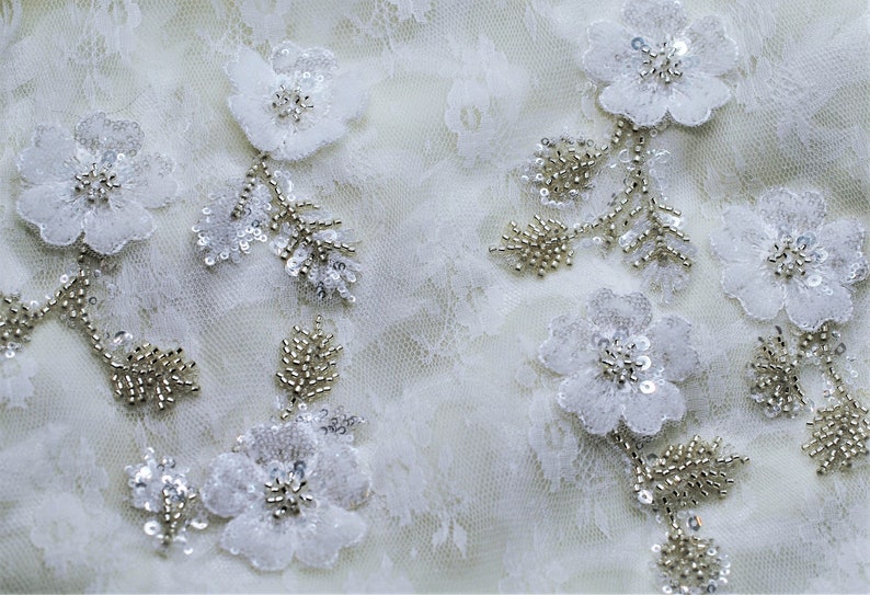 May include: White lace fabric with delicate floral appliques and silver beading.