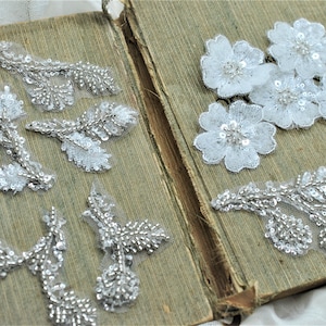 May include: Assortment of white lace appliques with silver beading and sequins. Some appliques are floral shapes and others are leafy branches.