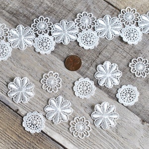 May include: White lace trim with a floral design. The trim is arranged in a row with individual lace flowers scattered below.