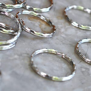 May include: A collection of silver-colored, textured metal rings. The rings have an irregular, organic shape and are scattered across a light-colored surface. The rings appear to be key rings or jewelry components.