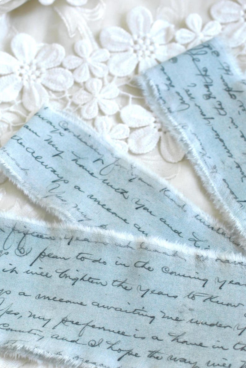 May include: Three strips of light blue fabric with frayed edges, featuring dark gray cursive handwriting printed across the surface. The text includes phrases such as 'always a welcome' and 'brighten the years to know'. The fabric has a soft texture.