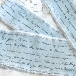 May include: Three strips of light blue fabric ribbon with frayed edges, featuring dark blue cursive handwriting printed across the surface. The text includes phrases such as 'always a onecome awaiting me under your' and 'my preference is a home'.
