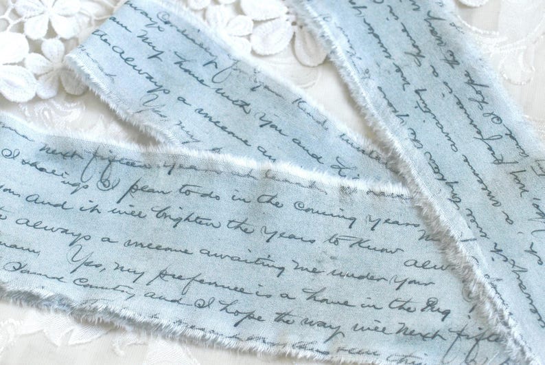 May include: Three strips of light blue fabric ribbon with frayed edges, featuring dark blue cursive handwriting printed across the surface. The text includes phrases such as 'always a onecome awaiting me under your' and 'my preference is a home'.