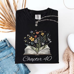 May include: Black t-shirt with a floral design and an open book with the text "Chapter 40".