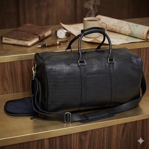 Könnte beinhalten: Eine schwarze Leder-Reisetasche mit Krokodiltextur, mit einem oberen Griff und einem abnehmbaren Schultergurt. Ein Notizbuch, ein Stift, eine Uhr und eine Tasse Kaffee befinden sich auf der Oberfläche. Eine Karte ist im Hintergrund aufgerollt.