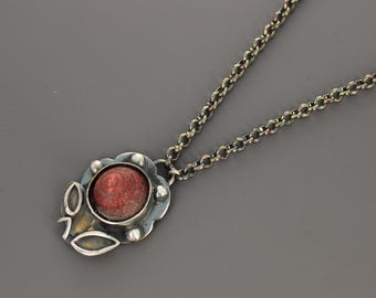 May include: A necklace featuring a dark oxidized silver chain and a pendant shaped like a flower. The center of the flower contains a small, conical, textured red shell. The silver petals and leaves surrounding the shell have a darkened finish.