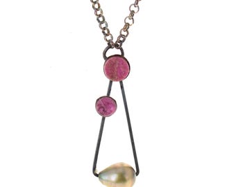 May include: A necklace featuring a dark metal chain and a triangular pendant frame. The pendant includes two small, round, magenta-colored stones and one teardrop-shaped, iridescent, light-colored pearl suspended at the base of the frame.