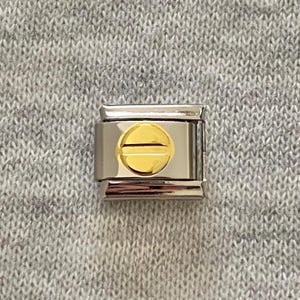 Op de afbeelding: Een rechthoekige modulaire bedelarmbandschakel met een gepolijst zilverkleurig metalen frame en een centraal cirkelvormig goudkleurig accent met een horizontale lijn die door het midden loopt.