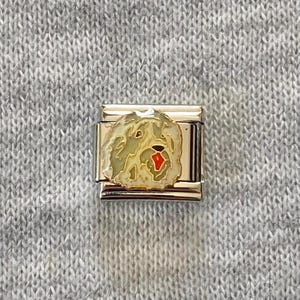 Könnte beinhalten: Ein rechteckiges, modulares Gliederelement aus Edelstahl mit einer cremefarbenen Emaille-Einlage, die ein zotteliges Hundegesicht mit einer kleinen roten Nase zeigt. Das Metallglied hat eine polierte, silberfarbene Oberfläche.