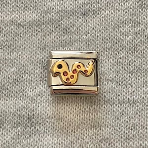 May include: A rectangular silver-tone modular link charm featuring a polished metallic finish. Centered on the link is a raised gold-tone snake figure with a smooth surface and small, evenly spaced red circular accents along its winding body.