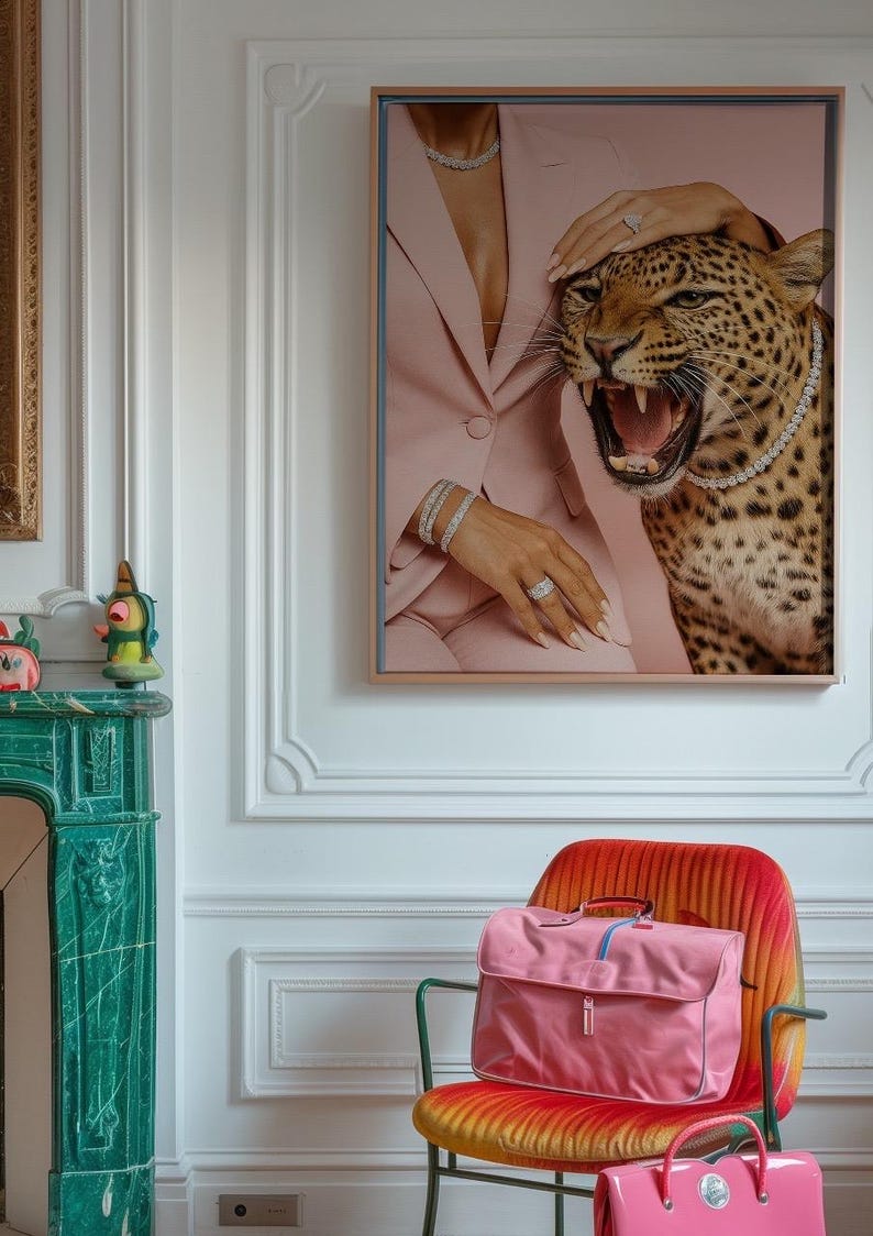 May include: A framed artwork depicts a woman in a pink suit with a bejeweled leopard. A pink satchel and a smaller pink handbag sit on a colorful chair. The room features a green fireplace and white walls.