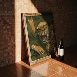 May include: A framed artwork featuring a woman in a green blazer with diamond jewelry, alongside a snarling leopard. A bottle of wine with a blank label leans against the frame. The setting is a tiled floor and wall.