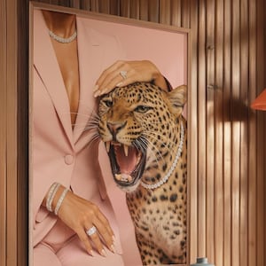 May include: A framed artwork featuring a roaring leopard wearing a diamond necklace. The artwork also shows a person in a pink blazer and diamond jewelry. The background is a pink hue.