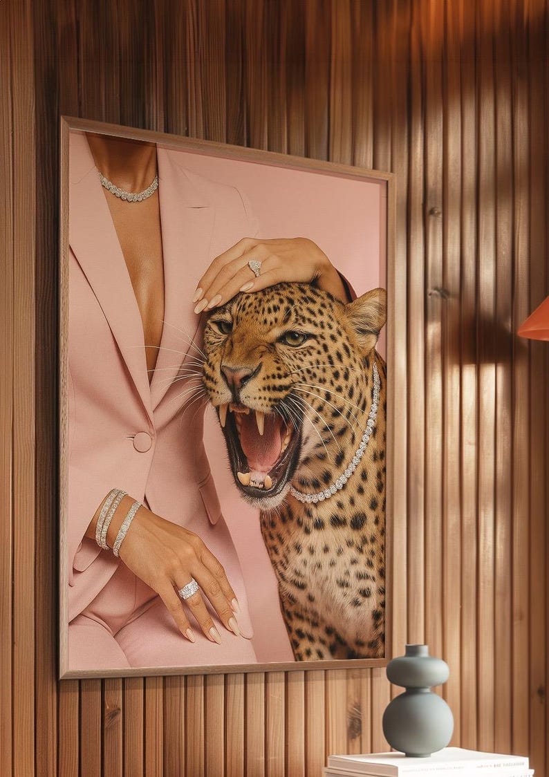 May include: A framed artwork featuring a roaring leopard wearing a diamond necklace. The artwork also shows a person in a pink blazer and diamond jewelry. The background is a pink hue.