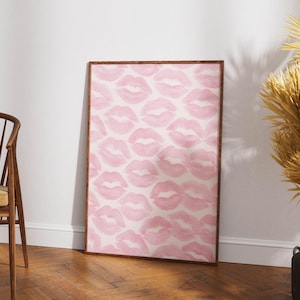 May include: A framed art print featuring a pattern of pink lips on a white background. The artwork is displayed in a room with a wooden floor and a wooden chair. The print has a brown frame.