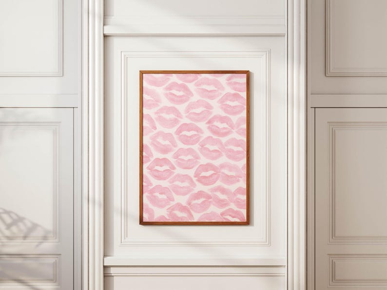May include: A framed print featuring a pattern of pink lips on a white background. The artwork is displayed in a room with white trim and a wooden frame. The lips are in a repeating pattern.