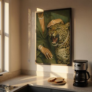 May include: A framed art print featuring a woman in a green blazer with diamond jewelry, posing with a snarling leopard. The leopard wears a pearl necklace. The artwork is displayed in a kitchen setting with a coffee maker and a cutting board with bread.