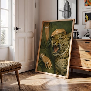 May include: A framed art print featuring a woman in a green suit with a leopard. The leopard is wearing a pearl necklace and has its mouth open. The woman is wearing jewelry, including a bracelet, ring, and necklace. The artwork is in a wooden frame.