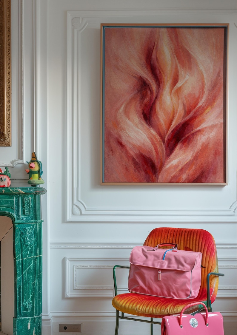 May include: An abstract painting in a wooden frame hangs above a vibrant orange chair. A pink satchel bag with a blue stripe sits on the chair. The room features a green fireplace and white walls.