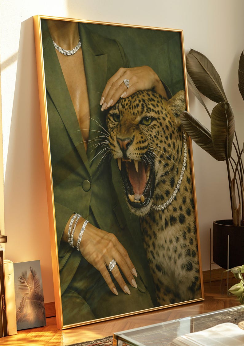 May include: Framed artwork featuring a leopard with an open mouth, adorned with a diamond necklace. The artwork includes a person wearing a green blazer and diamond jewelry. The frame is gold.