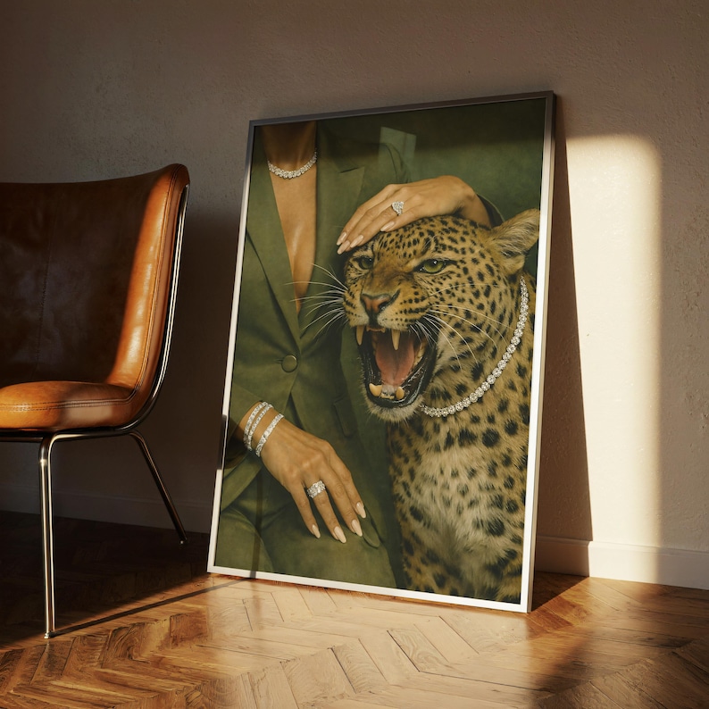 May include: A framed art print featuring a leopard with an open mouth, wearing a diamond necklace, and a person in a green suit. The person is wearing diamond jewelry. The artwork is displayed next to a brown leather chair.