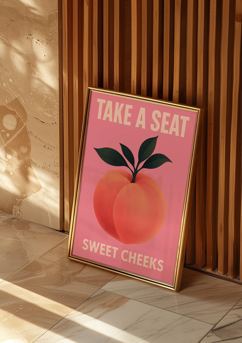 Puede incluir: Impresi&oacute;n art&iacute;stica enmarcada con fondo rosa, con una ilustraci&oacute;n de melocot&oacute;n y el texto "TAKE A SEAT SWEET CHEEKS" en blanco. El melocot&oacute;n es de un naranja-rosa vibrante con hojas verdes. El marco es dorado.