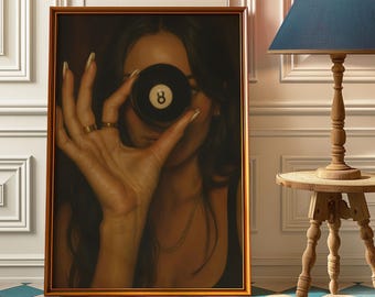 May include: Framed art print featuring a close-up of a person holding a black eight ball in front of their face. The print has a gold frame and is displayed against a white wall. The image has a vintage aesthetic.