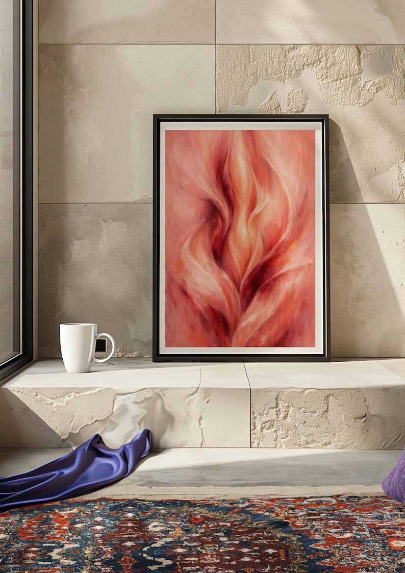May include: Framed abstract art print with a black border. The artwork depicts a flowing, flame-like design in red and peach hues. A white mug is on a ledge beside the framed art. A blue fabric and patterned rug are also visible.