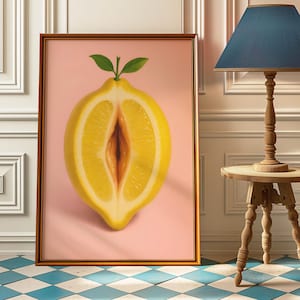 Op de afbeelding: Een ingelijste kunstdruk met een realistische afbeelding van een gehalveerde citroen tegen een roze achtergrond. De citroen is geel met een bruin interieur en heeft groene bladeren aan de bovenkant. Het kunstwerk wordt gepresenteerd op een blauw-witte geblokte vloer.