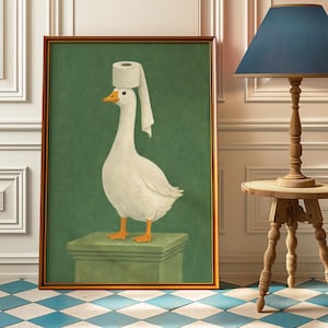 May include: Framed print of a white goose with a toilet roll on its head, standing on a green pedestal against a green background. The artwork has a humorous theme and is presented in a gold frame.