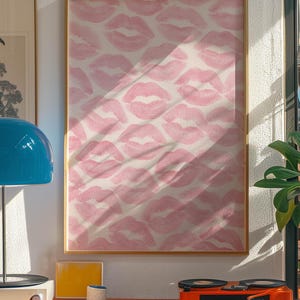 May include: A framed artwork featuring a repeating pattern of pink lipstick kiss prints on a white background. The artwork is displayed on a wall, with a red shelf below holding a record player, a lamp, and other decorative items.