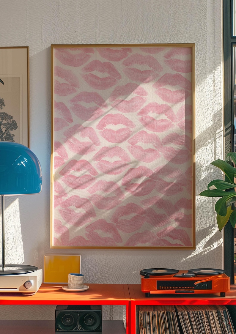 May include: A framed artwork featuring a repeating pattern of pink lipstick kiss prints on a white background. The artwork is displayed on a wall, with a red shelf below holding a record player, a lamp, and other decorative items.