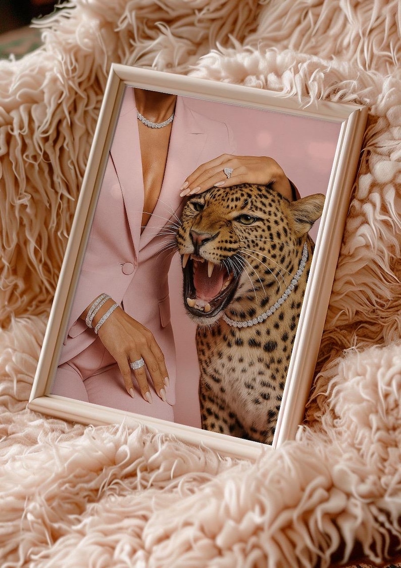 May include: Framed artwork featuring a leopard wearing a diamond necklace, with a woman in a pink suit and jewelry. The leopard's mouth is open, and the artwork is set against a pink background and a fluffy, peach-colored surface.