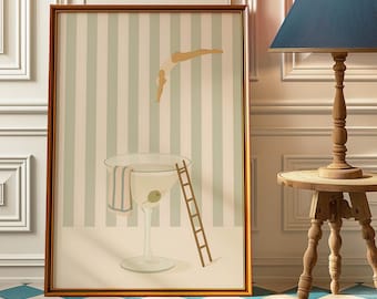May include: A framed art print depicts a whimsical scene of a diver plunging into a giant martini glass. The artwork features a ladder, an olive, and a striped towel, set against a striped background. The frame is a warm brown color.