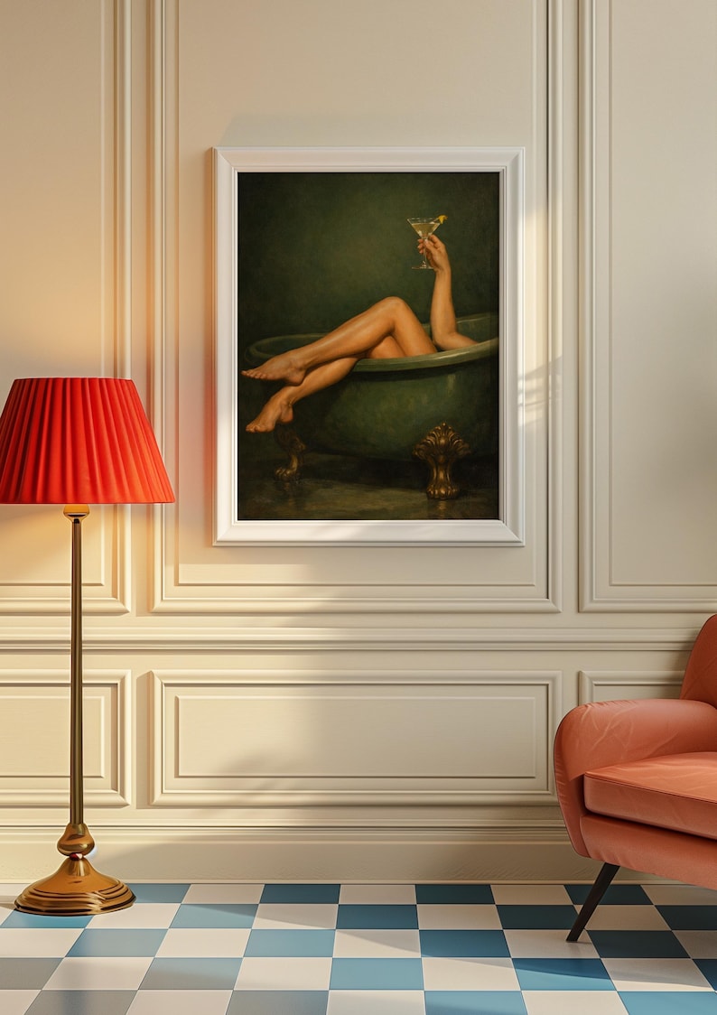 May include: A framed print depicts a person relaxing in a green clawfoot bathtub, holding a cocktail. The artwork is set against a dark green background. A red lampshade and a peach-colored armchair are in the foreground.
