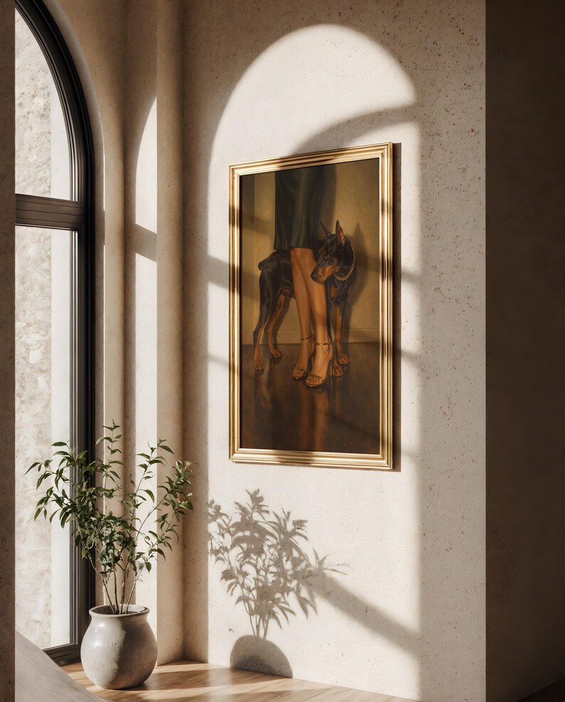 May include: A framed artwork featuring a Doberman Pinscher standing next to a person's legs and feet. The painting has a gold frame and is displayed on a textured wall. The scene is illuminated by natural light.