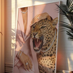 May include: A framed art print featuring a roaring leopard wearing a diamond necklace. The leopard's head is positioned next to a person wearing a pink blazer and jewelry. The background is a soft pink.