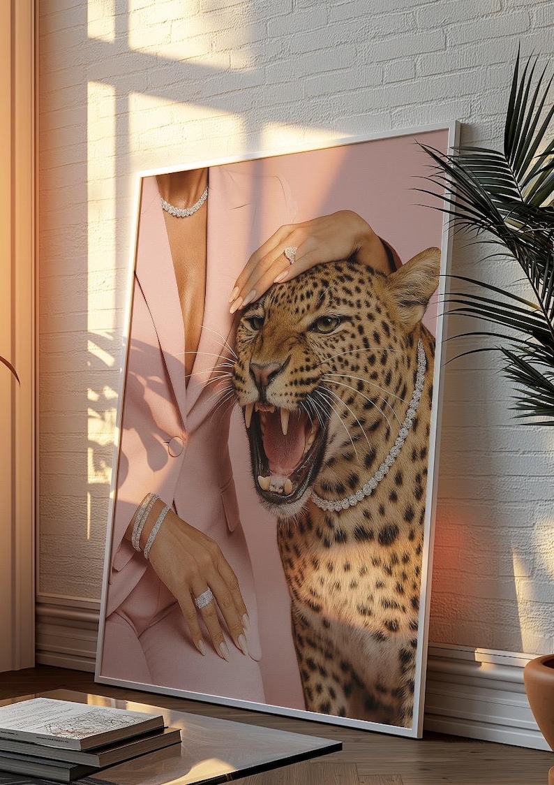 May include: A framed art print featuring a roaring leopard wearing a diamond necklace. The leopard's head is positioned next to a person wearing a pink blazer and jewelry. The background is a soft pink.