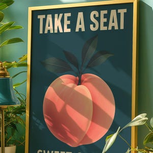 May include: Framed art print with a gold border. The artwork features a large peach illustration with the text "TAKE A SEAT SWEET CHEEKS" in gold lettering against a dark teal background.