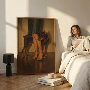 May include: A framed artwork featuring a Doberman Pinscher with a gold collar standing near a person's legs in high heels. The artwork is in a room with a black lamp, books, and a person in pajamas.