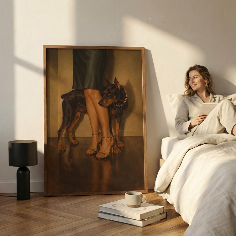 May include: A framed artwork featuring a Doberman Pinscher with a gold collar standing near a person's legs in high heels. The artwork is in a room with a black lamp, books, and a person in pajamas.