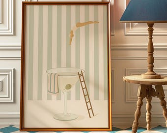 May include: A framed art print featuring a martini glass with a ladder and a person diving into the drink. The artwork has a light green and white striped background and a brown frame. An olive is in the martini.