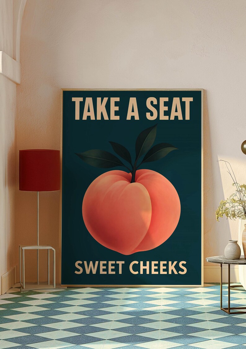 May include: A framed art print with a large peach illustration. The text "TAKE A SEAT SWEET CHEEKS" is in white on a dark teal background. The peach is a vibrant orange-red colour with green leaves. The artwork is a humorous piece.